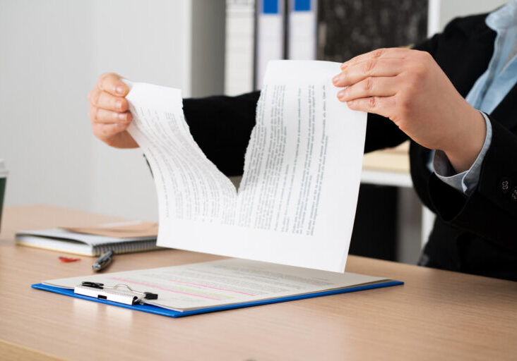 Close-up of the hands of a businesswoman tearing up the signed contract document sitting at a desk in the office